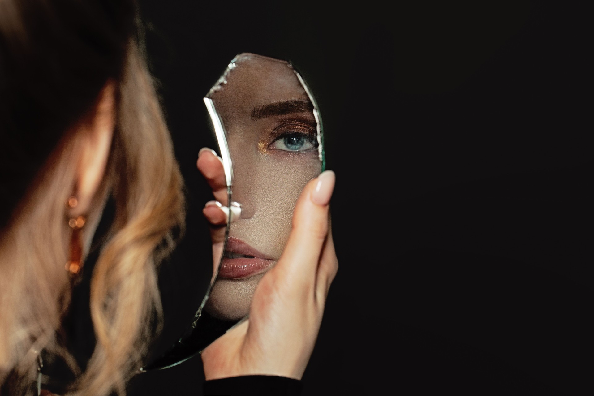 Young perfect woman holding broken self-image mirror on black background